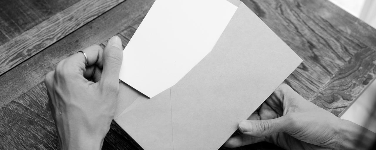Mãos tirando uma folha de um envelope, sobre uma mesa de madeira