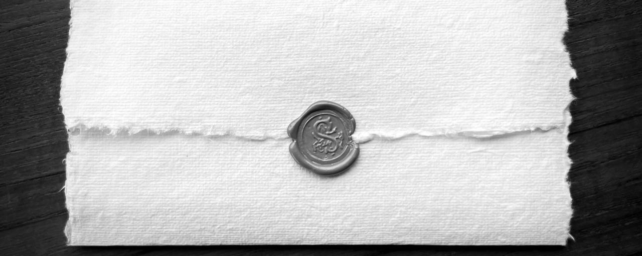 Envelope de papel artesanal fechado com selo de lacre, sobre uma mesa de madeira
