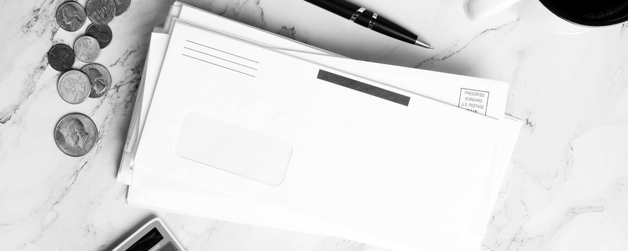 Moedas e envelopes em branco ao lado de uma calculadora, sobre mármore