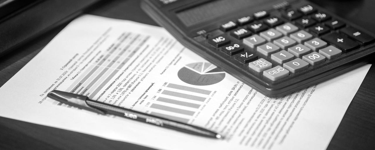 Calculadora sobre um relatório financeiro com gráficos e uma caneta, numa mesa de madeira